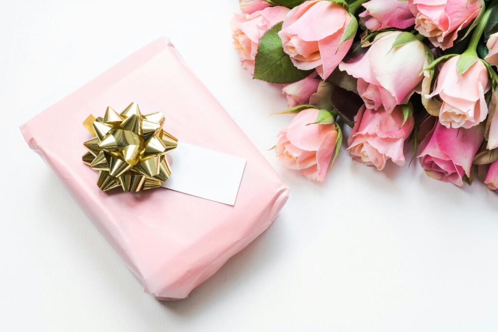 Elegant arrangement of pink roses with a beautifully wrapped gift box featuring a golden bow.