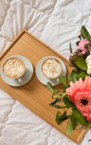 Cozy morning scene with coffee on a wooden tray and fresh flowers on a duvet.