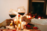 Close-up of a couple toasting with red wine glasses in a romantic candlelit setting.