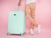 A fashionable studio shot of a person with pastel luggage and trendy ripped jeans against a pink background.