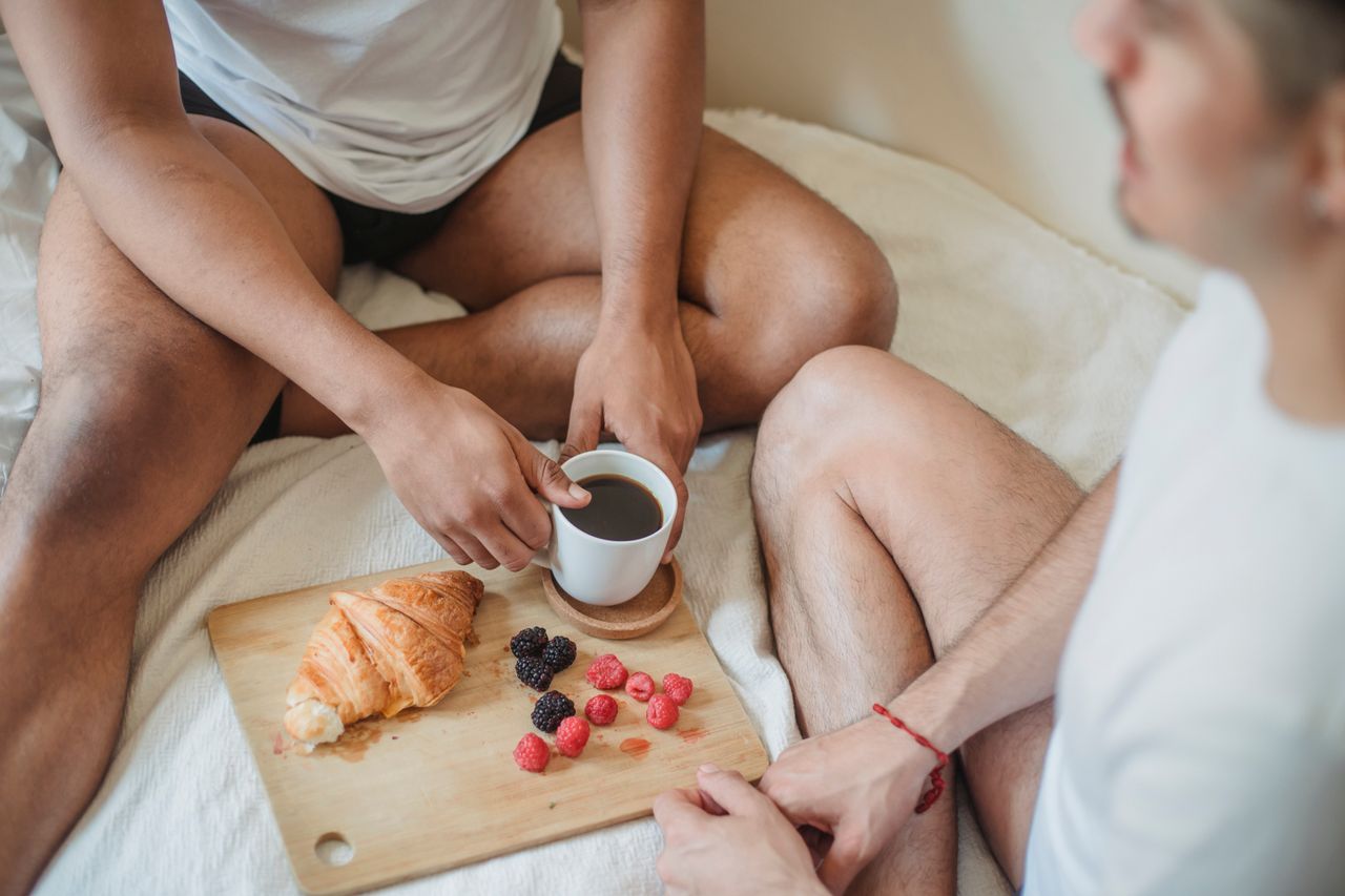 Two people enjoying a relaxed breakfast in bed with pastries and coffee.